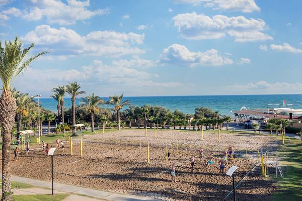 Sandvolleyballplatz im Asteria Family Resort Belek mit mehreren Spielern und Palmen.