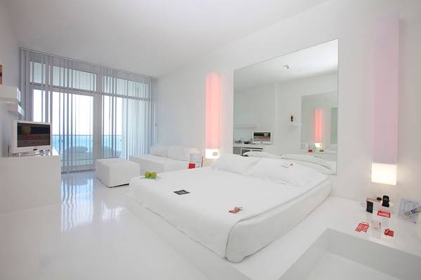 Schlafzimmer im Su Hotel mit weißem Bett, Spiegel, Fernseher und moderner Einrichtung.