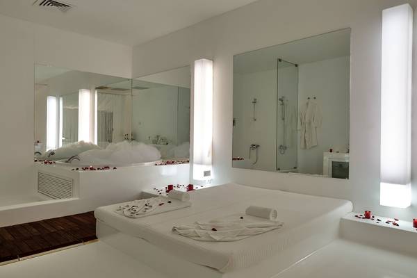 Ein elegantes Hotelschlafzimmer mit einer weißen Badewanne, Spiegeln und roten Rosenblättern.