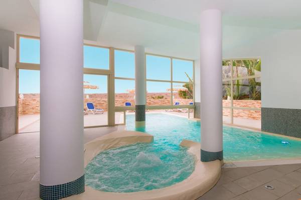 Innenpool im VOI Praia De Chaves Resort mit Sonnenliegen und Fenstern, die zum Außenbereich führen.