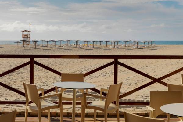 Ausblick auf den Strand des VOI Praia De Chaves Resort mit mehreren Tischen und Stühlen auf der Terrasse.