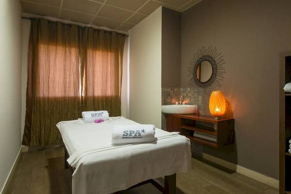 Spa-Behandlungsraum im VOI Praia De Chaves Resort mit einer Massageliege, einem Waschbecken, einem Spiegel und einer Lampe.