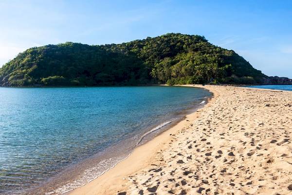 Eine Sandstrand mit klarem Wasser und einem Berg im Hintergrund.