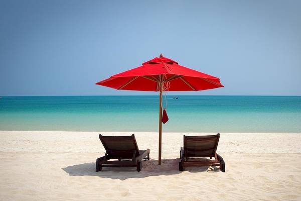 Zwei Liegen unter einem roten Sonnenschirm am Strand