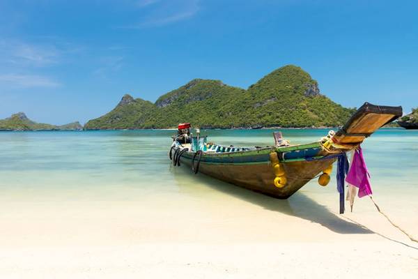 Ein Boot liegt am Strand von Koh Phangan mit Bergen im Hintergrund.