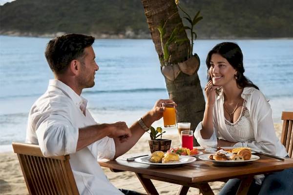 Ein Paar sitzt am Strand und isst im Anantara Rasananda Koh Phangan Villas.