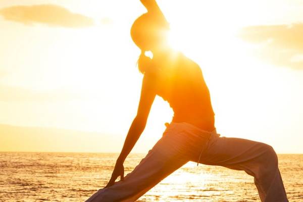 Person praktiziert Yoga am Strand bei Sonnenaufgang mit Blick auf das Meer