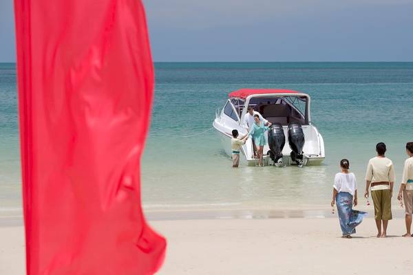 Familie am Strand von Anantara Rasananda Koh Phangan Villas mit einem Boot im Hintergrund