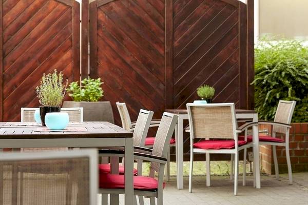 Terrasse des NH Hamburg Altona Hotels mit Tischen und Stühlen, Pflanzen und Holzwänden.