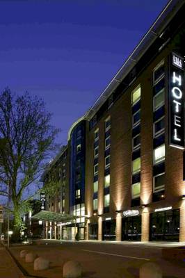 NH Hamburg Altona Hotel bei Nacht mit Beleuchtung und Bäumen vor dem Gebäude.