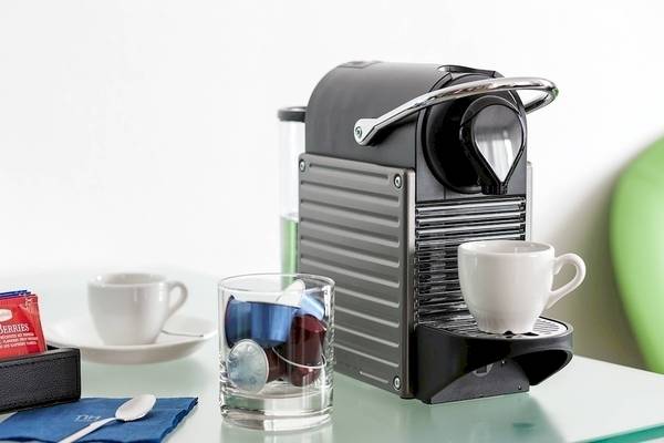 Kaffeemaschine des NH Hamburg Altona auf einem Tisch mit Tassen und Kaffeekapseln.