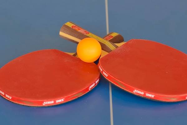 Zwei rote Tischtennisschläger mit einem gelben Ball auf einem blauen Tisch