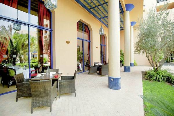 Terrasse des Atlas Medina & Spa Hotels mit blauen Säulen und Tischen im Freien.