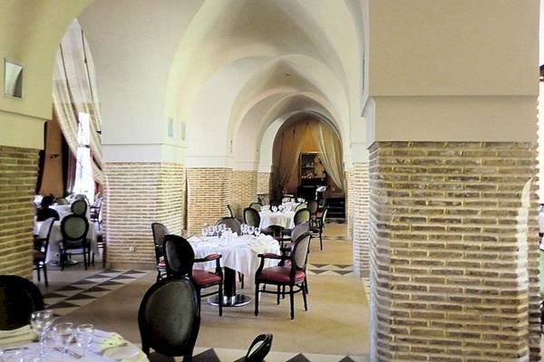 Innenansicht des Restaurants im Atlas Medina & Spa Hotel mit geschwungenen Decken, Ziegelwänden und runden Tischdecken.
