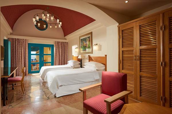 Innenansicht eines Hotelzimmers mit zwei Betten, Tisch, Stuhl, Kleiderschrank und Aussicht auf den Garten