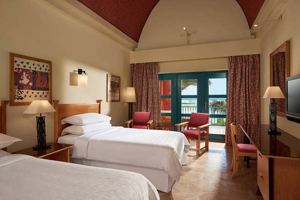 Doppelzimmer mit Meerblick im Sheraton Miramar Resort El Gouna, mit zwei Betten, einem Tisch, Stühlen und einem Fernseher.