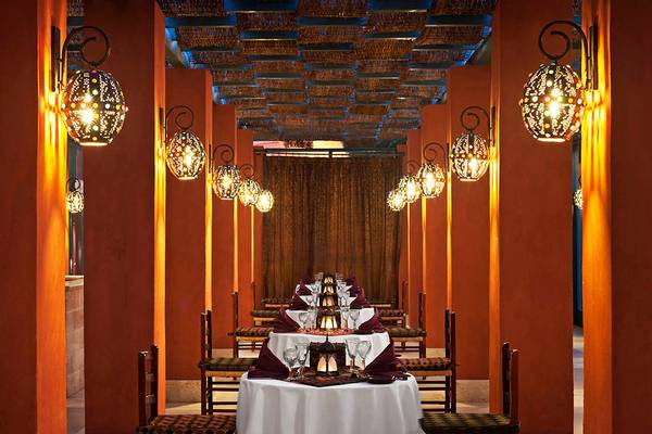 Eine Reihe von orangefarbenen Säulen im Sheraton Miramar Resort El Gouna mit hängenden Laternen und einem langen Tisch.