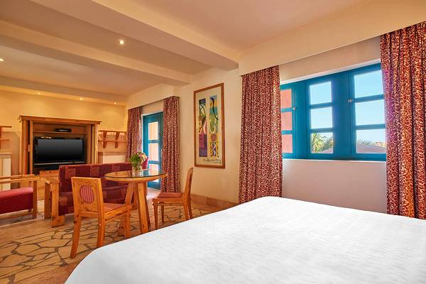 Hotelzimmer mit Doppelbett, Tisch, Stühlen, Fernseher und roter Vorhang
