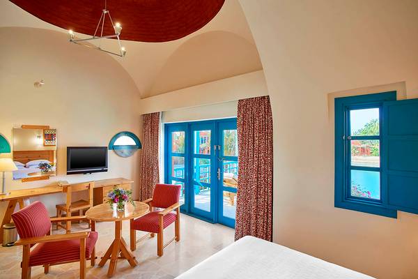 Innenansicht eines Zimmers im Sheraton Miramar Resort El Gouna mit einem Bett, einem Schreibtisch, einem Fernseher und einem Balkon.