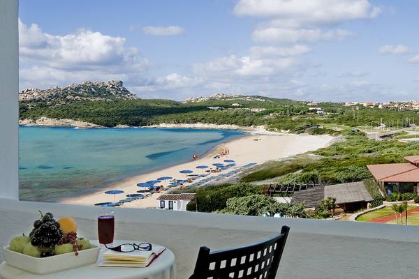 Aussicht auf einen Strand vom Colonna Grand Hotel Capo Testa mit einer weißen Tischplatte, Obst, einem Glas Saft und einer Brille.