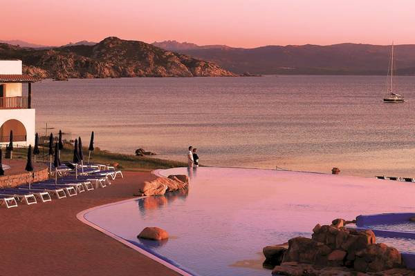 Abendlicher Ausblick auf das Wasser mit zwei Personen und einem Hotel im Hintergrund.