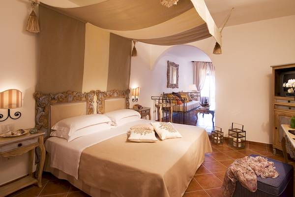 Schlafzimmer im Colonna Grand Hotel Capo Testa mit einem großen Bett, zwei Nachttischen und einer gemütlichen Atmosphäre.