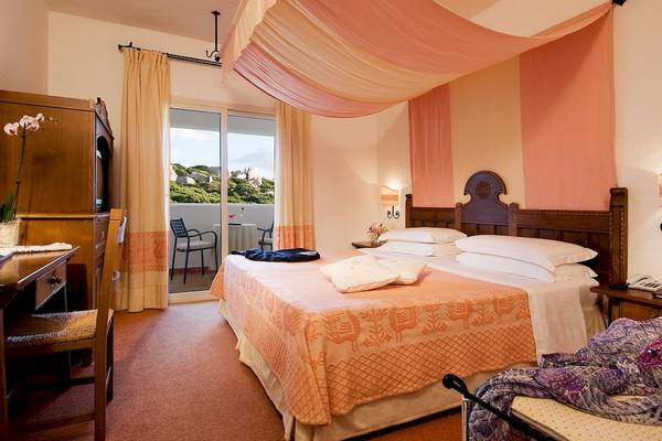 Doppelbett im Colonna Grand Hotel Capo Testa mit Blick auf einen Tisch auf dem Balkon.