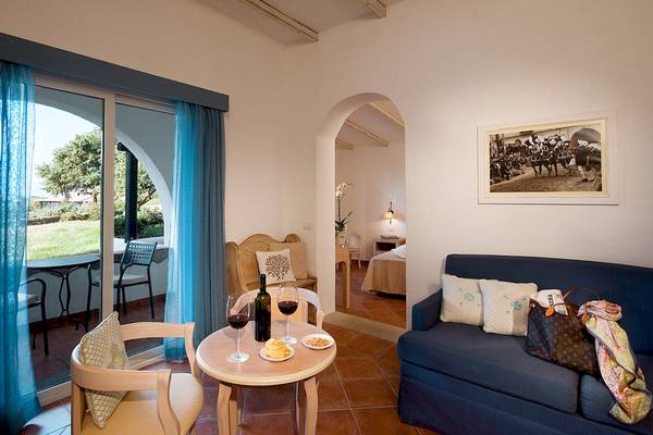 Hotelzimmer mit Tisch, Sofa, Wein und Kissen im Colonna Grand Hotel Capo Testa.