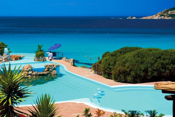 Luftaufnahme des Pools des Colonna Grand Hotel Capo Testa mit kristallklarem Wasser und umliegenden Pflanzen.