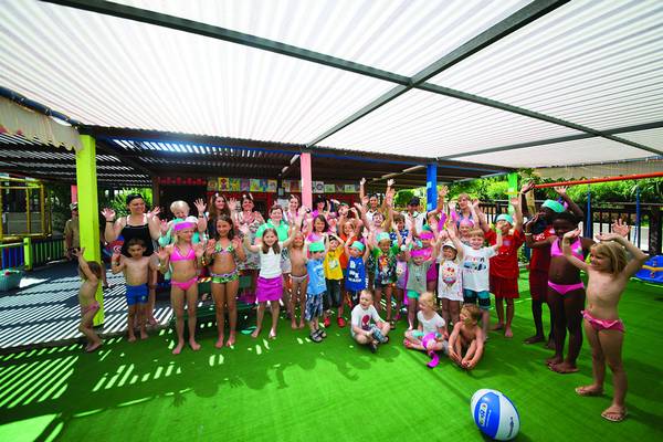 Gruppe von Kindern und Erwachsenen, die unter einem Dach mit Spielgeräten und Schattendach posieren.