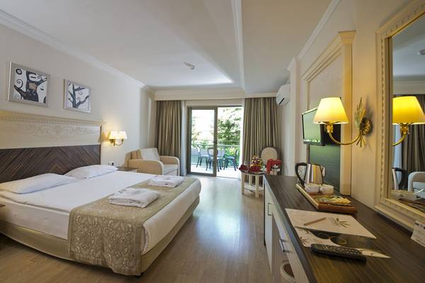 Innenansicht eines Hotelzimmers im Aydinbey Kings Palace & Spa mit Bett, Möbeln und Balkon.