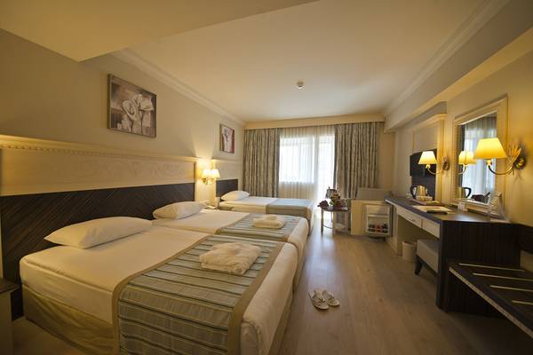 Hotelzimmer im Aydinbey Kings Palace & Spa mit drei Betten, Nachttischen und einem Schreibtisch.