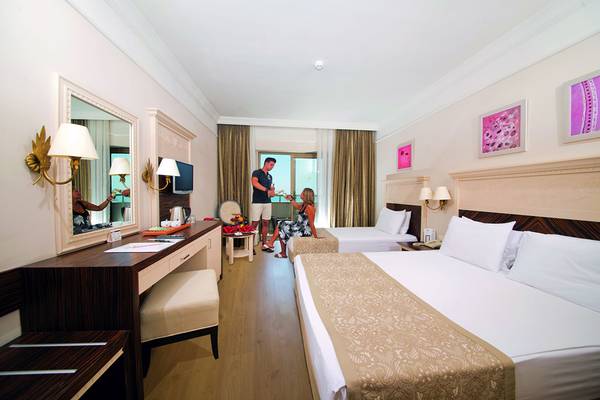 Zimmer im Aydinbey Kings Palace & Spa Hotel mit zwei Betten, Schreibtisch und Spiegel.
