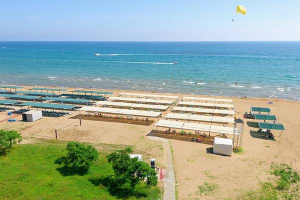 Luftaufnahme des Club Hotel Sidelya Strands mit Sonnenschirmen und Wassersport im Hintergrund.