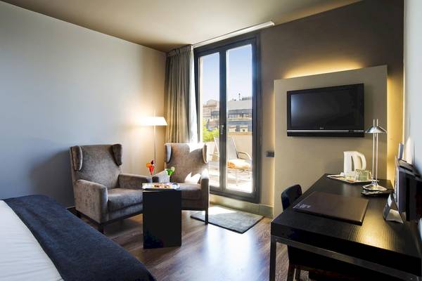 Innenansicht eines Zimmers im Gran Hotel Havana Barcelona mit Möbeln und Fernseher.