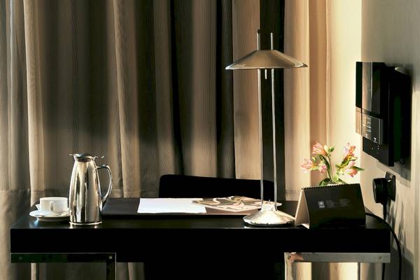 Arbeitsbereich im Zimmer des Gran Hotel Havana Barcelona mit Lampe, Tisch, Blumen, Tasse und Kalender.