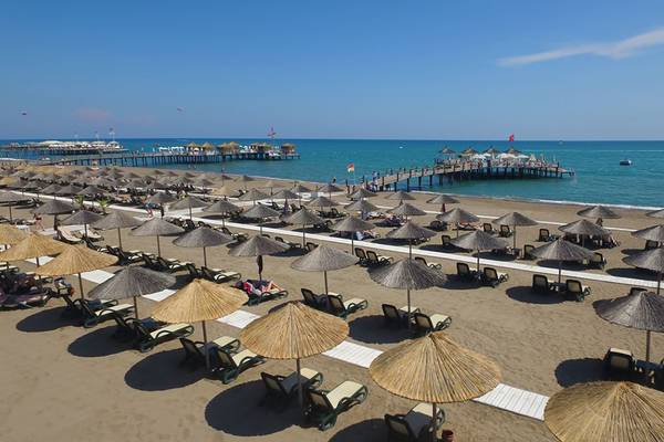 Strand des Baia Lara Hotels mit vielen Sonnenliegen und Sonnenschirmen, ein Pier im Hintergrund.