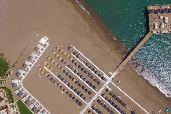 Luftaufnahme des Baia Lara Hotels mit Strand und Pier, vielen Sonnenschirmen und Liegen