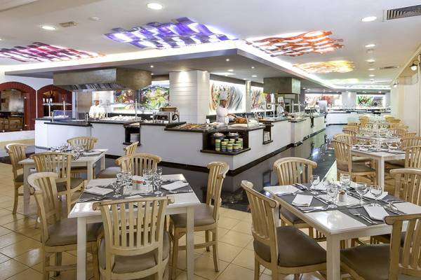 Innenansicht des Restaurants im Sol Palmeras Hotel mit gedeckten Tischen und Köchen hinter der Theke.