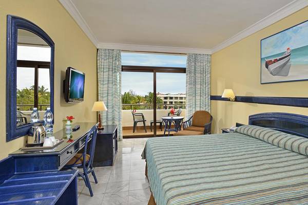 Innenansicht eines Hotelzimmers im Sol Palmeras Hotel mit Balkon, Fernseher, Schreibtisch und Gemälde.