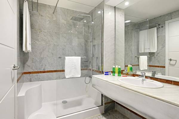 Badezimmer im Sol Palmeras Hotel mit Marmorfliesen, Badewanne, Dusche, Waschbecken und Spiegel.