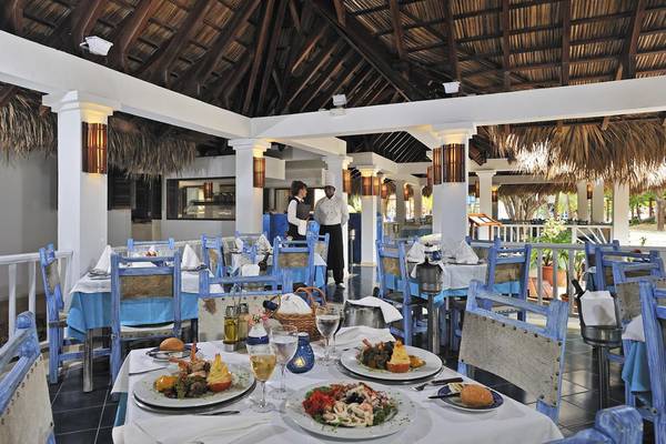 Restaurant im Sol Palmeras Hotel mit blauen Stühlen und Tischen, serviertem Essen und zwei Mitarbeitern im Hintergrund.