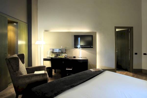 Innenansicht eines Zimmers im Gran Hotel Havana Barcelona mit Schreibtisch, Fernseher und Bett.