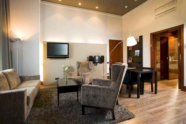 Wohnzimmer im Gran Hotel Havana Barcelona mit Sofa, Fernseher, Tisch und Stühlen.