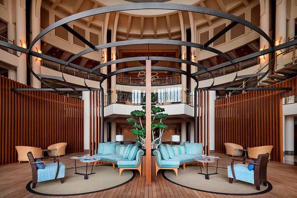 Lobby des Kempinski Hotel Barbaros Bay mit blauen Sofas, Holzwänden und zentralem Baum.