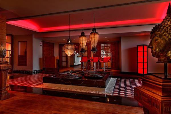 Innenansicht der Lounge im Kempinski Hotel Barbaros Bay Bodrum mit roten Beleuchtung, Holzboden, Buddha-Statue und roten Stühlen.