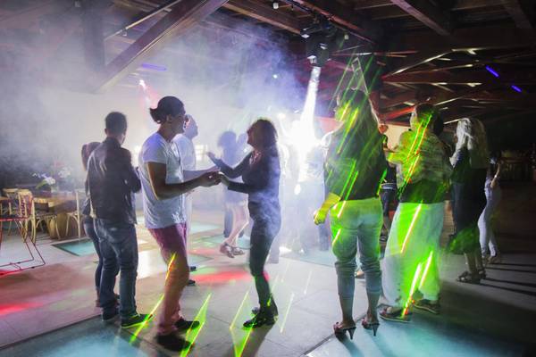 Mehrere Leute tanzen in einer Disco mit Lichteffekten und Rauch.
