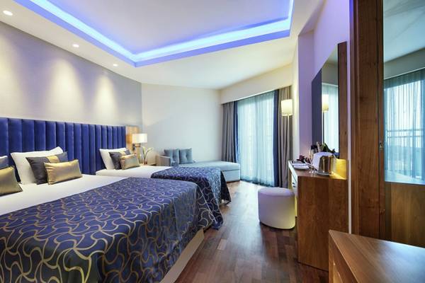 Hotelzimmer mit zwei Betten und Sofa, Dekor im Innenraum, blaue Kissen und Decken, Möbel und Fernseher.