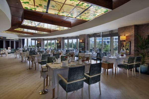 Innenansicht des Restaurants im Liberty Hotels Lara mit gedeckten Tischen und farbigen Deckenleuchten.