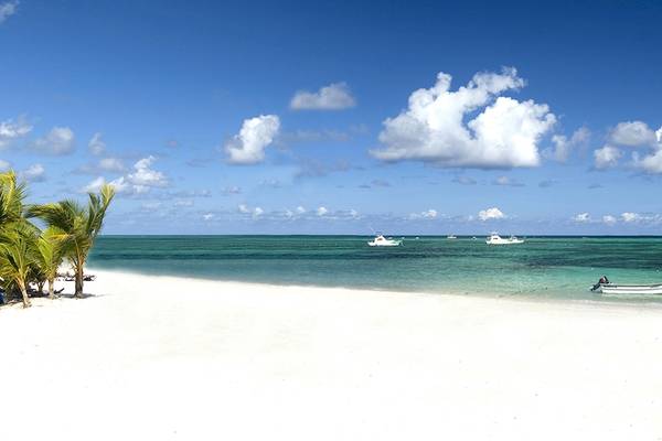 Strand des IFA Villas Bavaro Hotels mit weißen Palmen, Booten im Wasser und blauem Himmel.